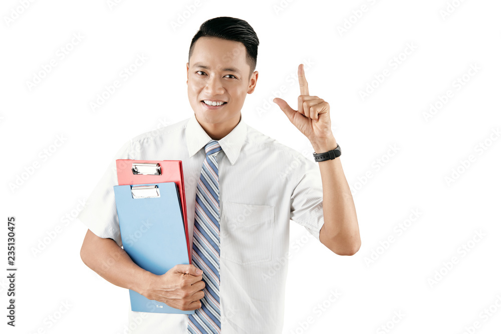 Portrait of young attractive Asian male office worker holding folders with papers, showing forefinger up and smiling at camera happily Portrait of young attractive Asian male office worker holding folders with papers, showing forefinger up and smiling at camera happily