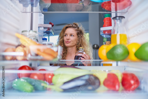 Woman standing in front of fridge full of groceries and looking for something to eat. Picture taken from the inside of fridge.