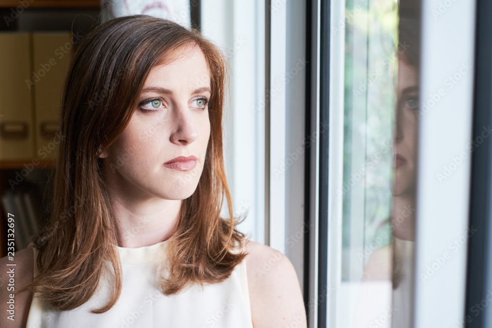 Beautiful serious woman standing near window looking pensively away in office