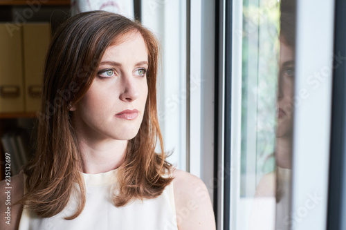 Beautiful serious woman standing near window looking pensively away in office