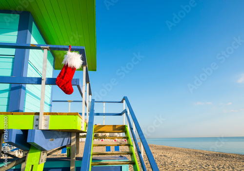 Fototapeta Naklejka Na Ścianę i Meble -  Santa stocking Christmas decoration hanging from brightly colored lifeguard tower next to calm tropical seas in Miami Beach, Florida, USA