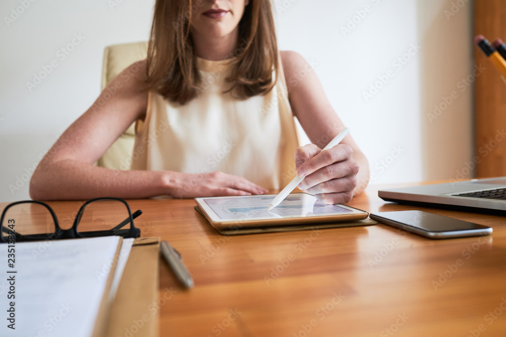 Crop businesswoman using tablet tapping it with stylus while working at table in office Crop businesswoman using tablet tapping it with stylus while working at table in office