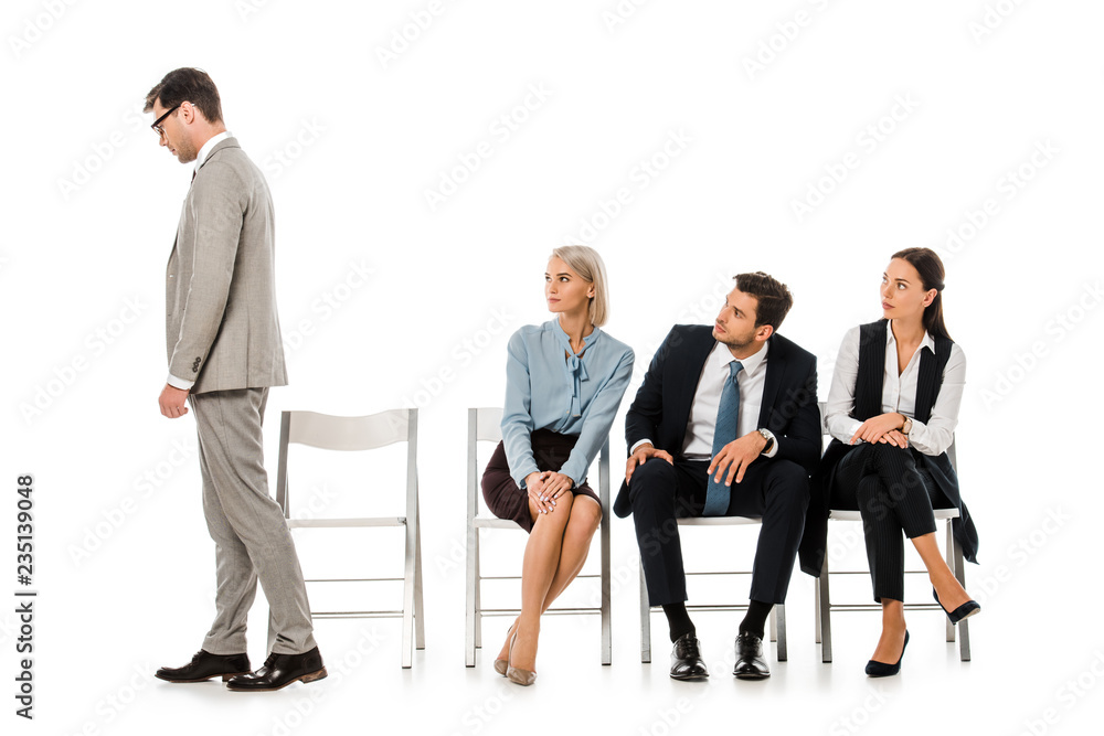 fired businessman going away while colleagues sitting on chairs and looking at him isolated on white fired businessman going away while colleagues sitting on chairs and looking at him isolated on white