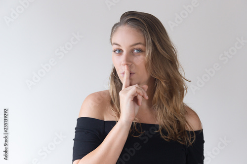 Obraz na plátně Positive pretty Caucasian woman holding finger near mouth