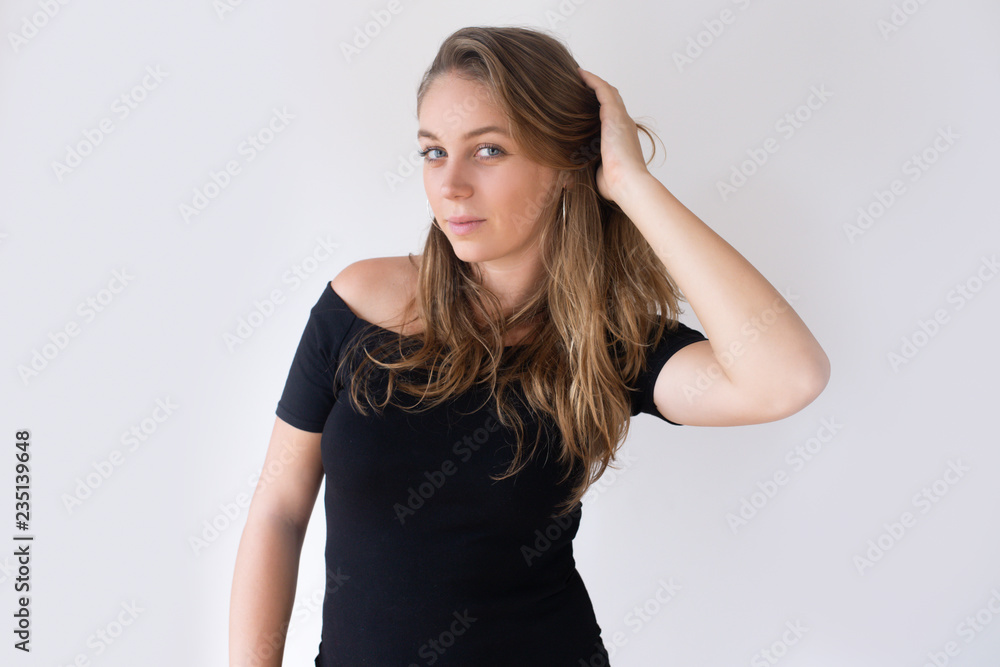 Pretty Caucasian girl holding hand behind head and brushing hair with fingers. Young woman in black dress checking her appearance. Mirror concept Pretty Caucasian girl holding hand behind head and brushing hair with fingers. Young woman in black dress checking her appearance. Mirror concept