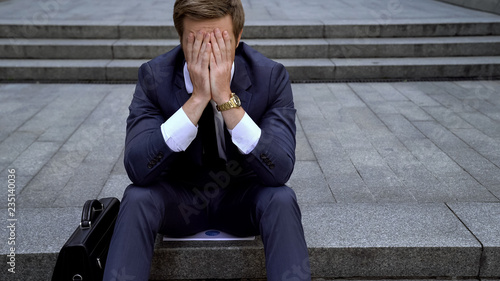 Desperate male sitting on ladder near building loosing all money on stock market photo