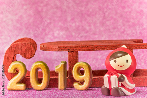 Pink glitter background for New Year's Cards with cute figurine of child in Christmas clothes with a present box in hands and handmade golden numbers of 2019 year. photo