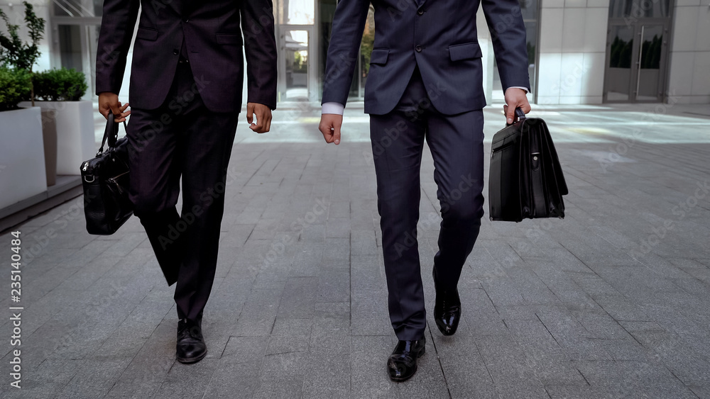 Determinate businessmen walking out office center holding briefcases cooperation Determinate businessmen walking out office center holding briefcases cooperation