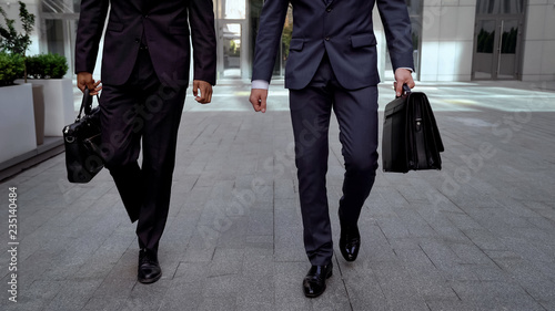 Determinate businessmen walking out office center holding briefcases cooperation