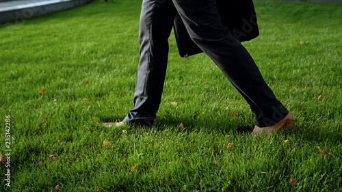 Young male in formal suit walking barefoot on green grass, relaxing after stress