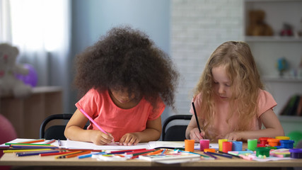 Two multi-racial girls drawing with colorful pencils in early education center