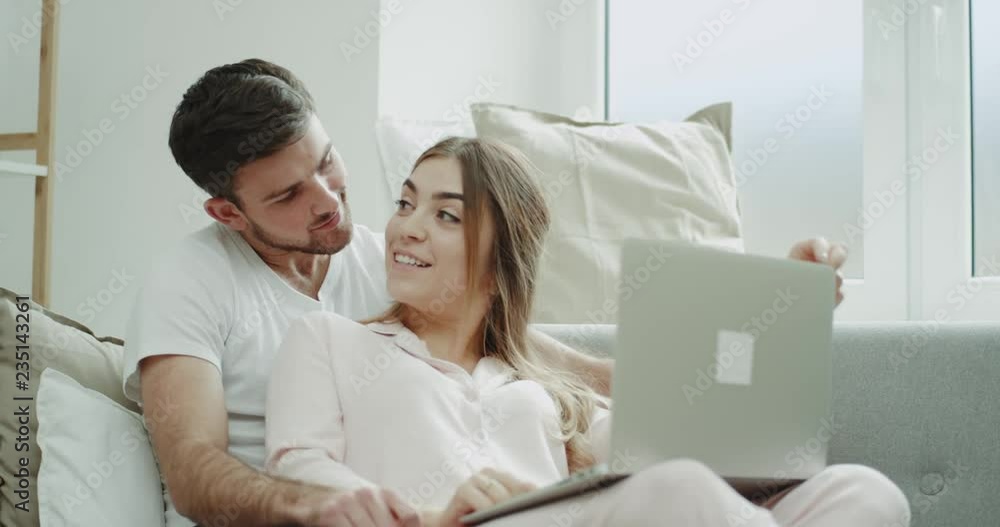 Portrait of young couple order something using a notebook sitting on sofa and both in pajamas Portrait of young couple order something using a notebook sitting on sofa and both in pajamas