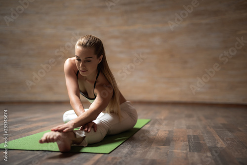 Calm relaxed lady doing yoga asanas and touching her toes while sitting on the yoga mat and practicing