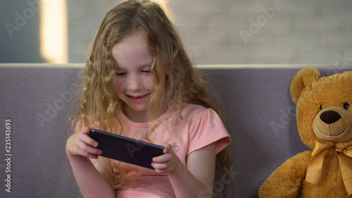 Photos Smiling little girl practicing math on smartphone app, early education software