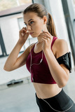 concentrated sportswoman in smartphone armband putting on earphones at gym