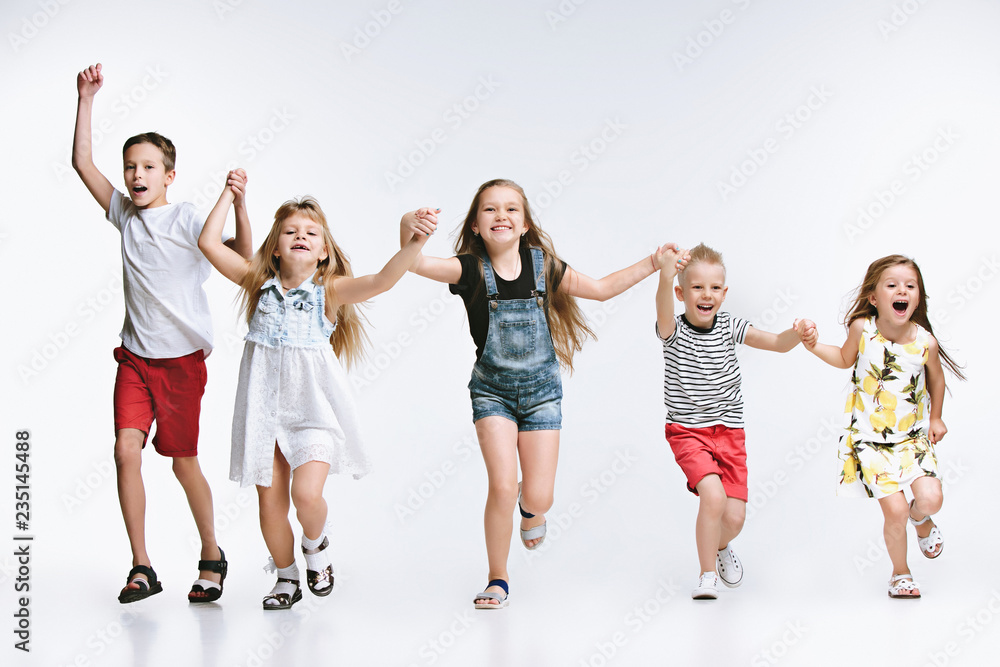 Obraz premium Group of fashion cute preschooler kids friends running together and looking at camera on a white studio background. The friendship, fashion, summer concept. Space for text.