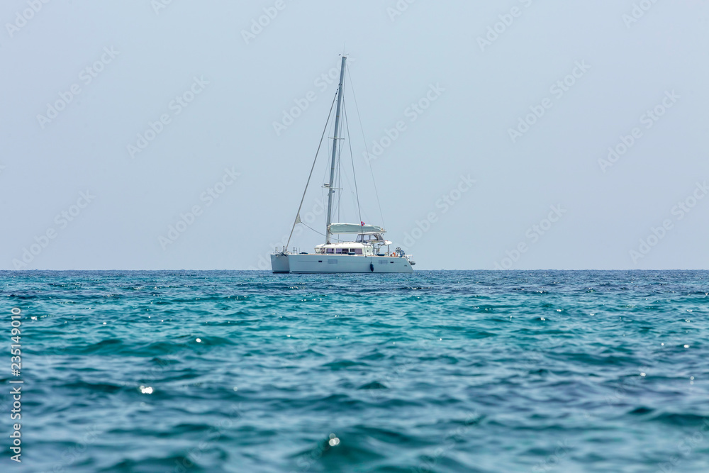 White sailing boat catamaran on ocean near beach.