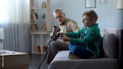 Foto Dissatisfied grandpa looking at happy grandson playing video game generation gap