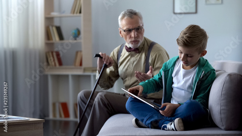 Konstfotografi Angry grandpa scolding grandson for playing video game on tablet, generation gap