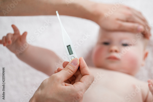 Close-up thermometer. Mother measuring temperature of her ill kid. Sick child with high fever laying in bed. Hand on forehead.