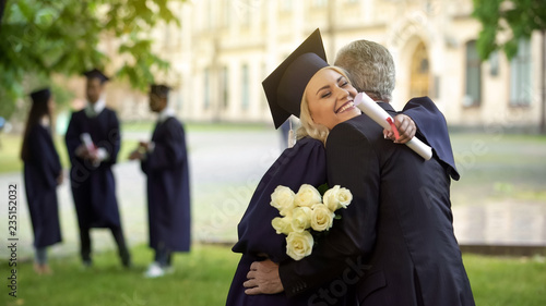 Obraz na płótnie Father hugging his graduate daughter giving flowers, congratulating, paternity