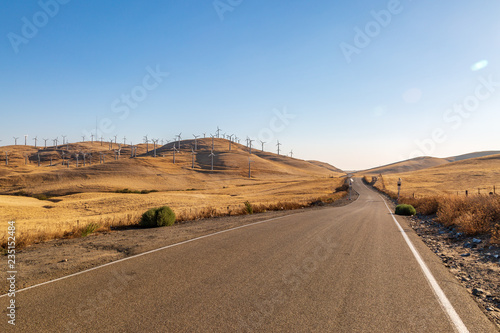 A road through the Californian countryside with a wind farm on the hills around