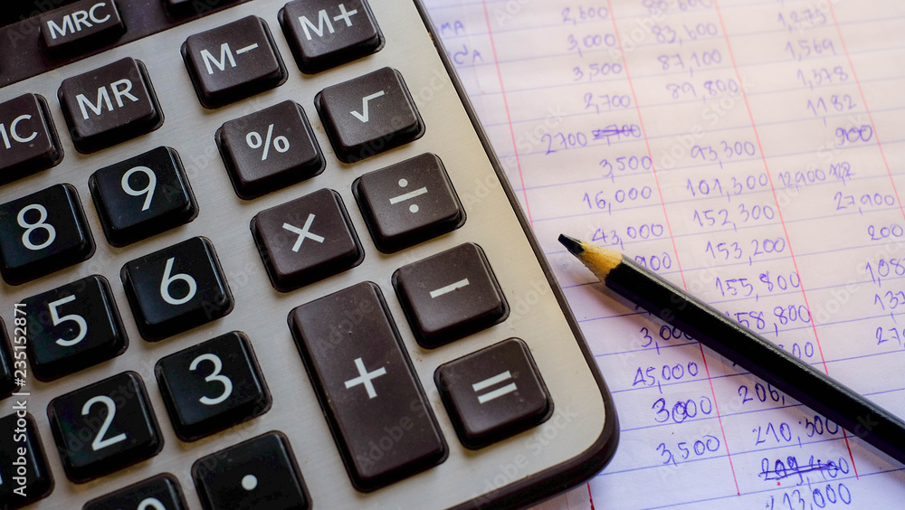 Calculator financial accounting on wood table and pencil book press button and coin. out of focus.