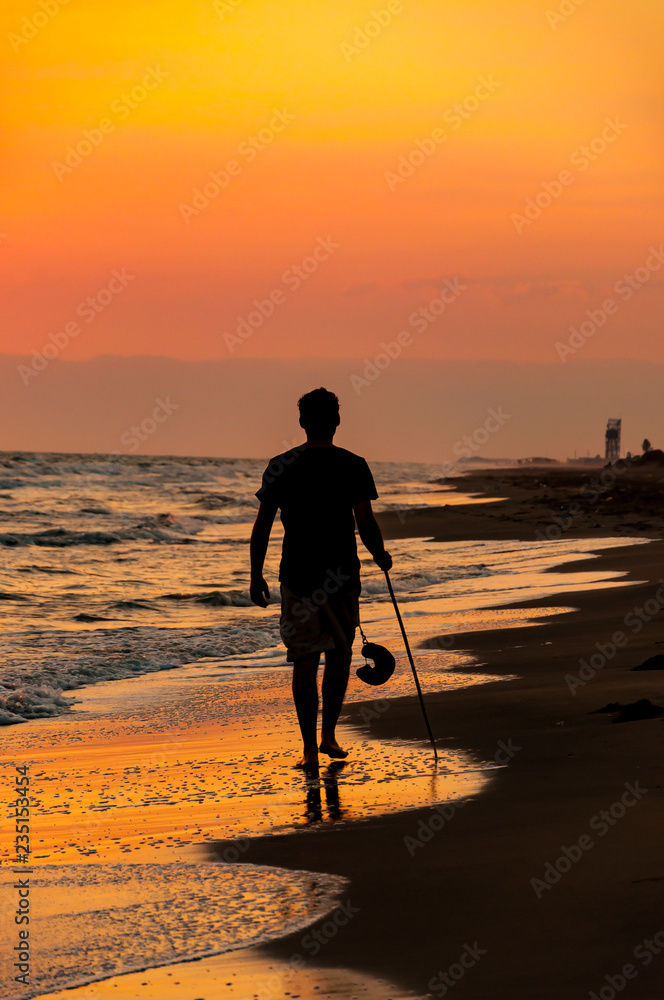 The man walking in beach at sunset with his hat and stick. Colorful background. The man walking in beach at sunset with his hat and stick. Colorful background.
