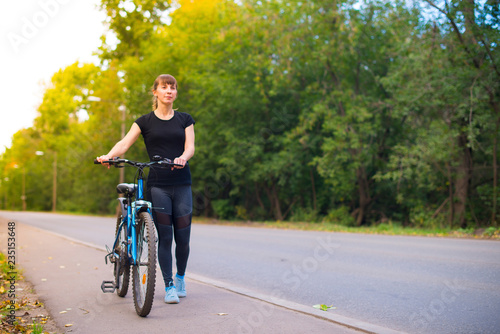 young beautiful girl leads the bike on the sidewalk