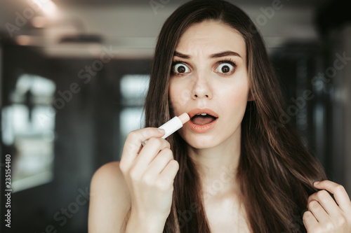 Portrait of shocked young female applying makeup while looking at camera. Attractive lady with perfect face concept
