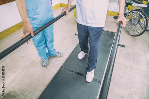 Disabled senior helped by the physiotherapist is doing rehabilitation on the footboard