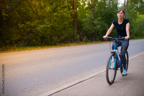 young beautiful girl in sportswear rides a blue bike on the sidewalk