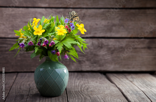 butterfly and bouquet of field wild flowers in a vase on old boards.