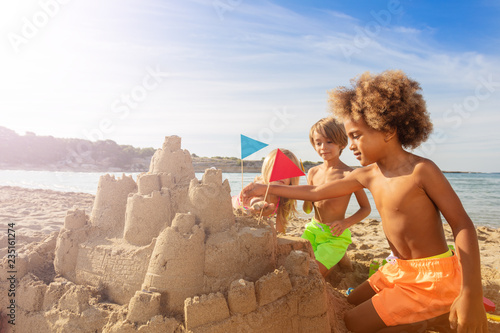 Happy kids decorating sandcastle towers with flags photo