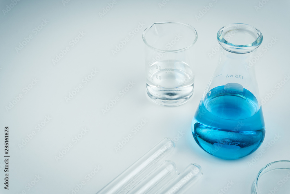 laboratory equipments. A blue liquid flask, clear liquid beaker, test tubes and petri dish on the white table laboratory equipments. A blue liquid flask, clear liquid beaker, test tubes and petri dish on the white table