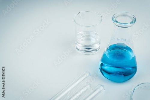 laboratory equipments. A blue liquid flask, clear liquid beaker, test tubes and petri dish on the white table