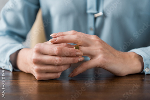 close-up partial view of woman taking off wedding ring, divorce concept