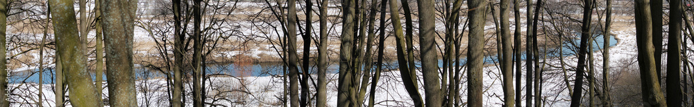 Panoramic early spring landscape. Snow-covered banks of river with trees. Svislach River in Loshitski Park Complex in Minsk, Belarus Panoramic early spring landscape. Snow-covered banks of river with trees. Svislach River in Loshitski Park Complex in Minsk, Belarus