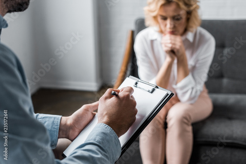 depressed woman having psychologist therapy session at office while therapist writing in clipboard