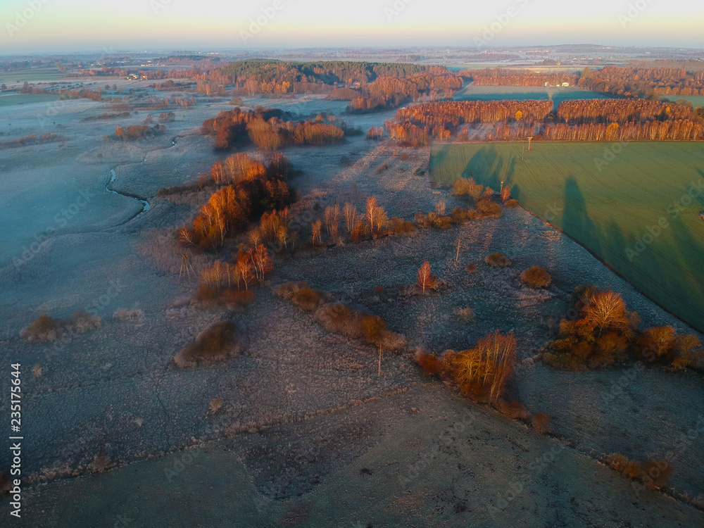 Aerial view on rising sun over frosted foggy valley divide by green meadow.