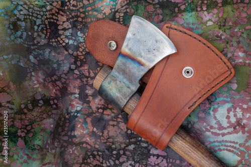 A leather sheath and hand forged tomahawk with color.