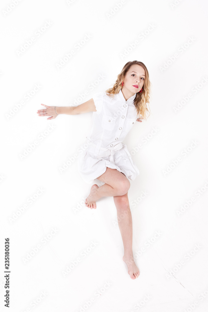 Fototapeta premium Pretty girl in white dress barefoot posing and dancing in studio on white bachground 20 years old