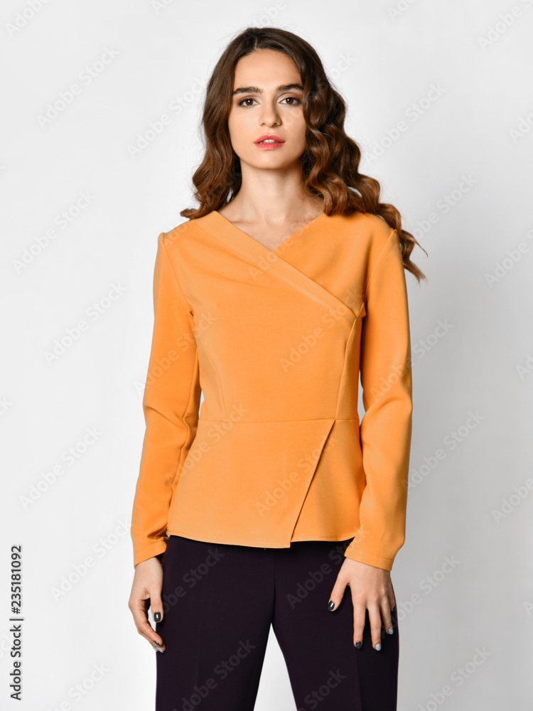 Young beautiful brunette woman posing in new casual yellow orange blouse sweater and black pants Young beautiful brunette woman posing in new casual yellow orange blouse sweater and black pants
