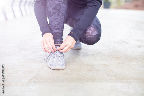 Sporty woman tying shoelace on running shoes before practice