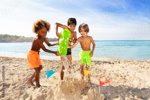 Happy boys making sandcastle together on the beach photo