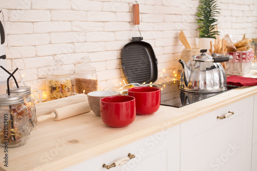Interior light kitchen with red decor and Christmas decorations. Preparing holiday dinner at home on the kitchen concept. Decorated new Year fir. Selective focus