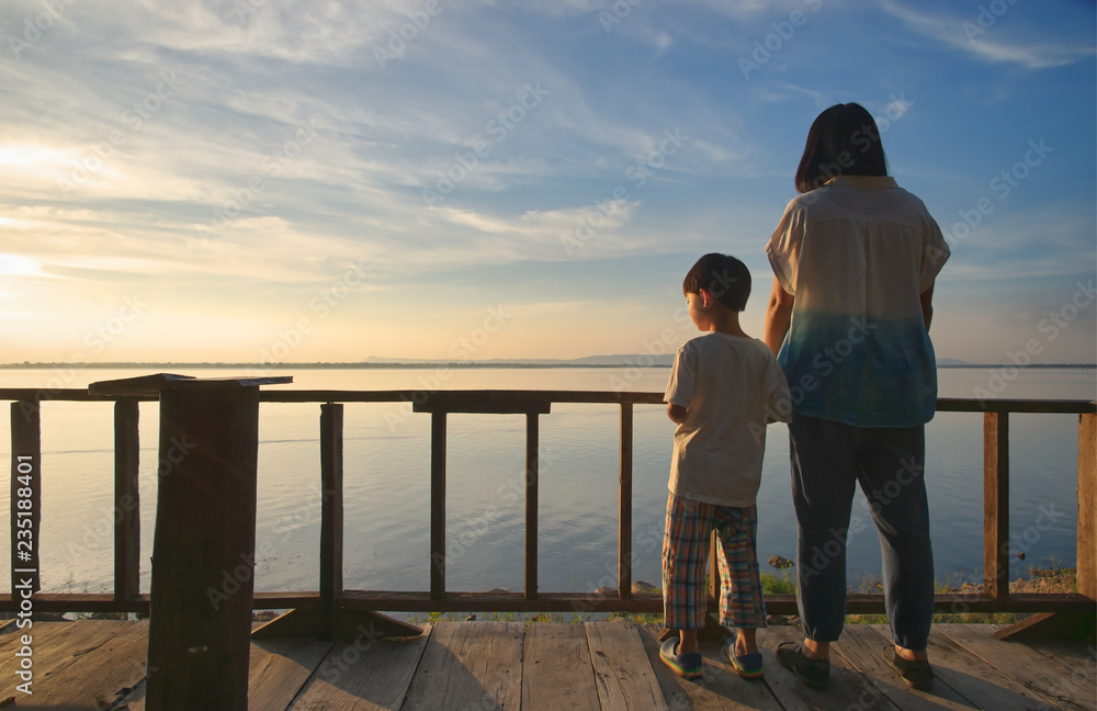 Fototapeta premium Mother and son on terrace looking at the lake and sunset sky : khonkaen, Thailand