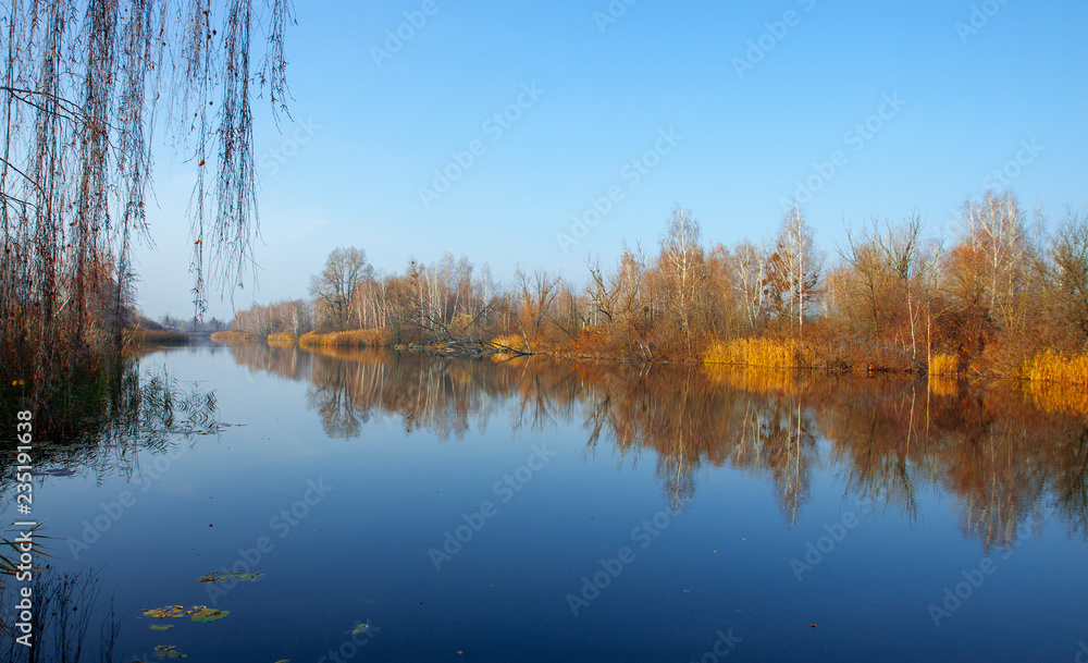 Beautiful autumn trees reflecting on the smooth water surface. Warm autumn day on the lake. River bank landscape. Beautiful autumn trees reflecting on the smooth water surface. Warm autumn day on the lake. River bank landscape.
