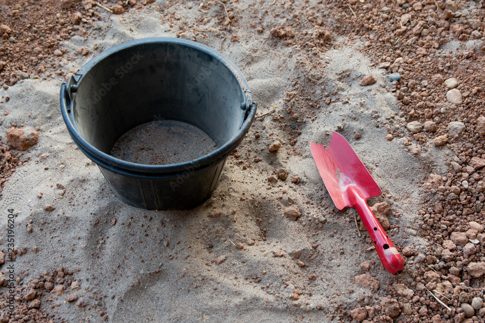 Red shovel and black Plastic bucket on sand Red shovel and black Plastic bucket on sand