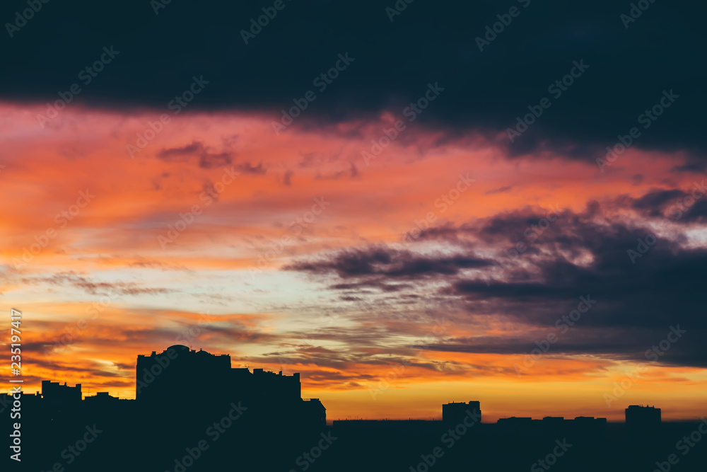 Cityscape with wonderful varicolored vivid dawn. Amazing dramatic multicolored cloudy sky above dark silhouettes of city buildings. Atmospheric background of sunrise in overcast weather. Copy space.